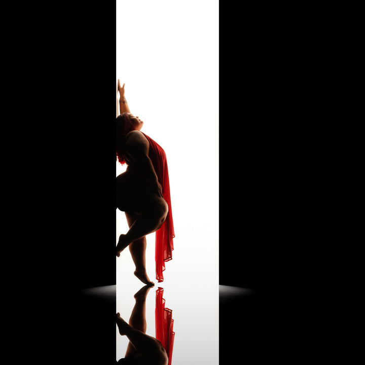 Backlit fine art silhouette of a woman in red chiffon reaching upward against a bright doorway of light