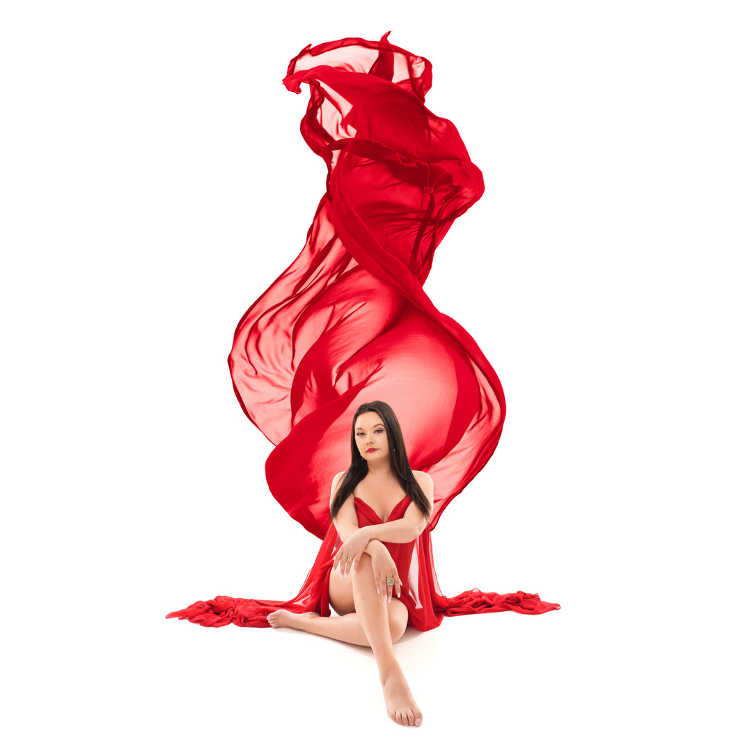 Retrato de boudoir artístico realizado por Nuovo Artistic Studios en el que aparece una mujer sentada, con una gasa roja que se extiende sobre su cabeza sobre un fondo blanco.