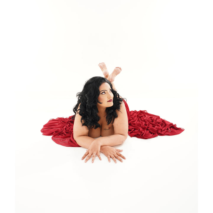 Woman wrapped in red fabric poses on a white studio floor for an elegant portrait.