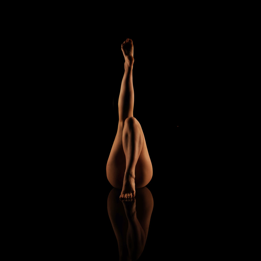 Fine art boudoir portrait of a woman’s legs posed against a black background with a dramatic floor reflection.