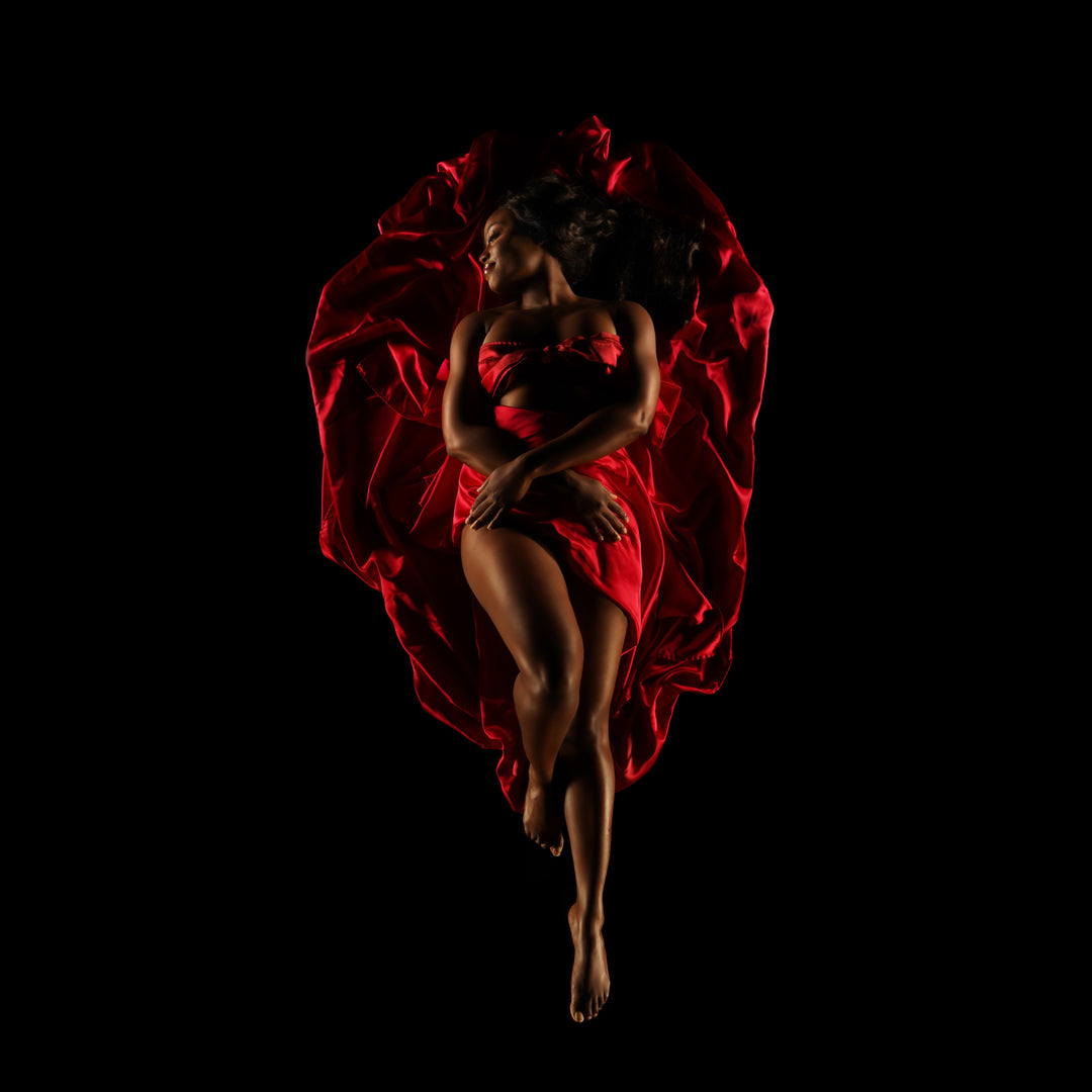 Woman surrounded by sculpted red fabric poses against a black background for a dramatic fine art boudoir portrait.