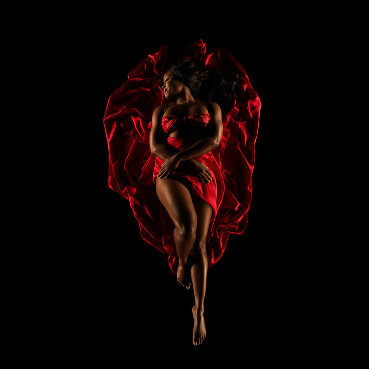 Woman surrounded by sculpted red fabric poses against a black background for a dramatic fine art boudoir portrait.