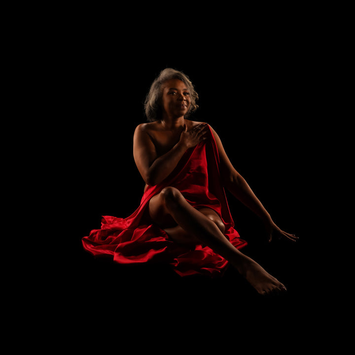 Low key fine art portrait of a woman with silver hair seated in red satin against a black backdrop
