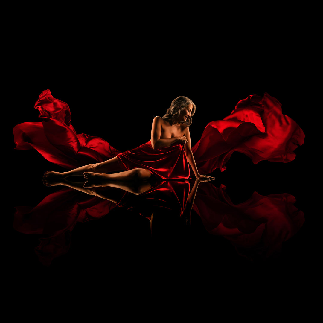 Woman surrounded by flowing red fabric poses on a reflective black floor for a dramatic fine art portrait.