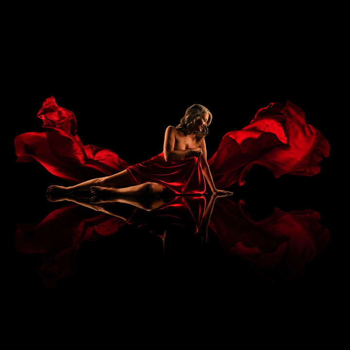 Woman surrounded by flowing red fabric poses on a reflective black floor for a dramatic fine art portrait.