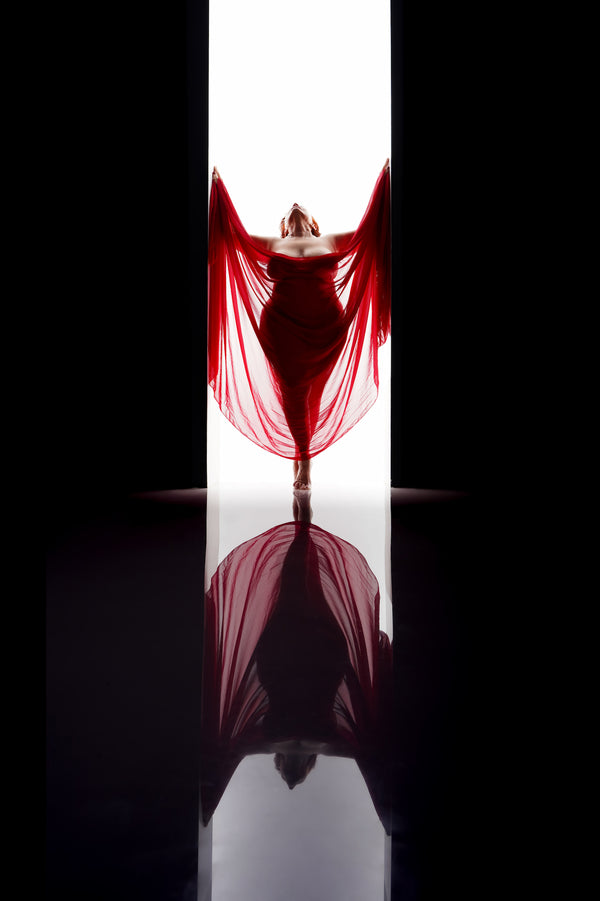 Timeless window shot capturing the essence of age-inclusive beauty, featuring an adult figure swathed in a flowing red fabric, backlit with a radiant glow and mirrored in the reflection on the floor, from Nuovo's Self-Love collection.